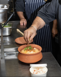 Chef garnishing a traditional clay pot biryani with fresh herbs.